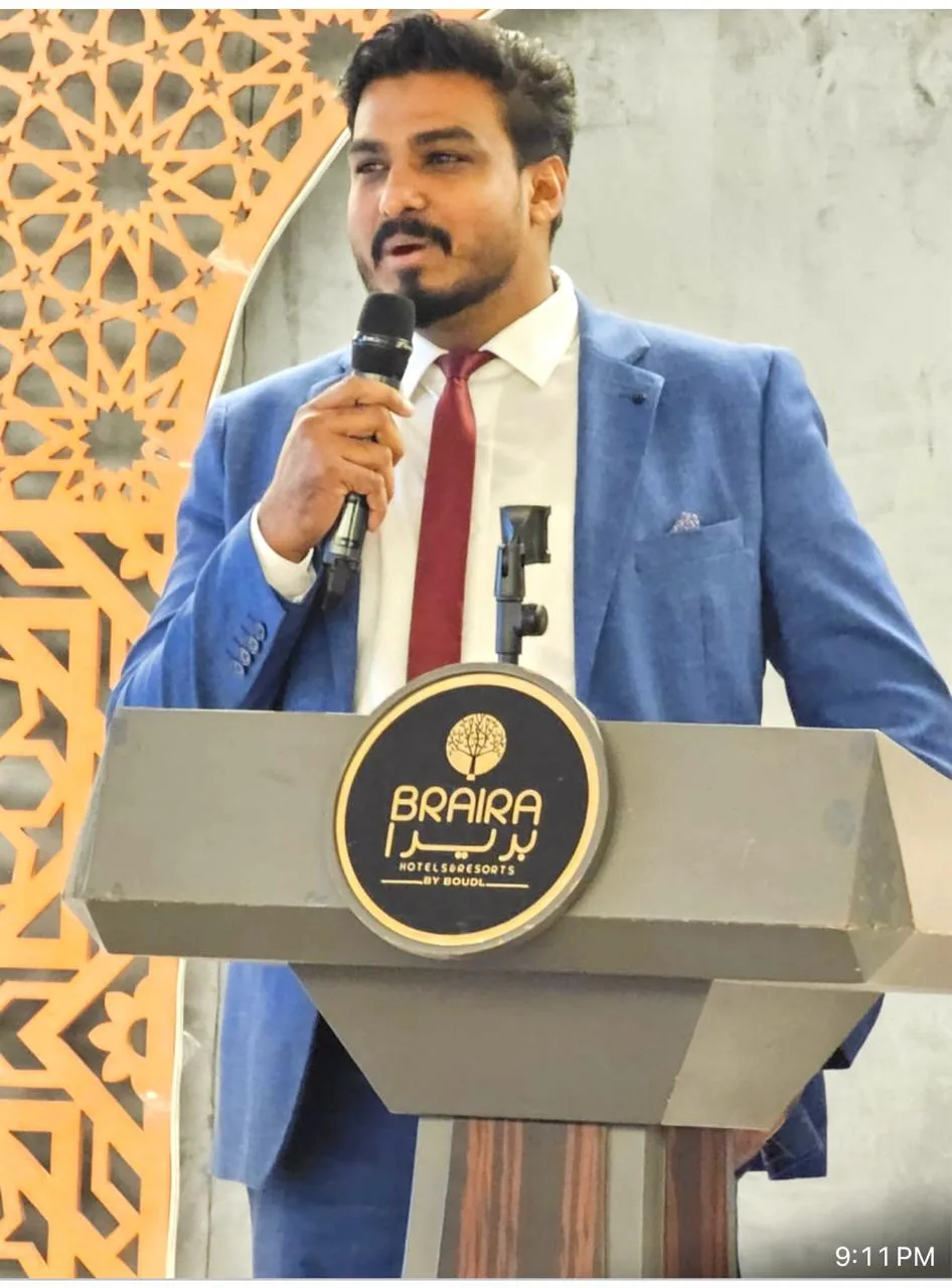 Rashin Hassan speaking at a business event, microphone in hand